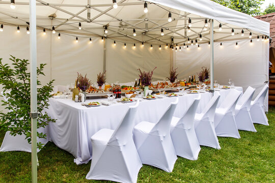 Wedding white tent with white chairs. Banquet hall under a tent for wedding or another catered event dinner