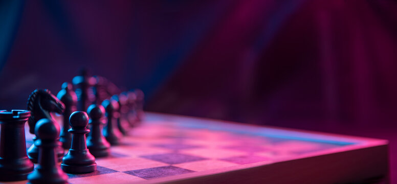 Chess pieces on a chessboard on a dark background shot in neon pink-blue colors. The figure of a chess .Close up.