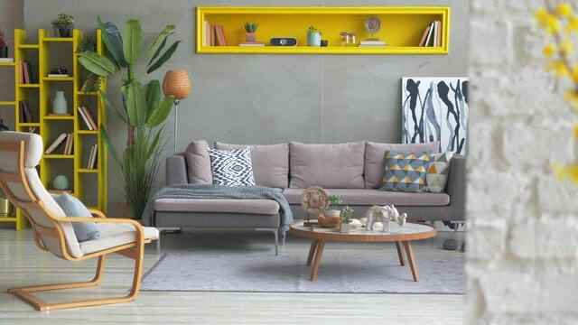 Grey corner sofa in the room with yellow niche, pillow, lamp, vase of plant, middle table, carpet, poster and rocking chair.