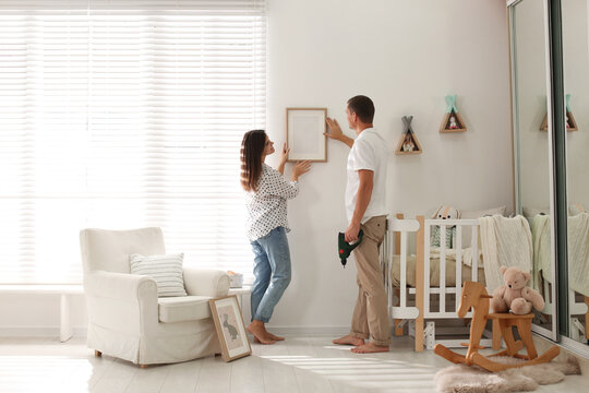 Happy couple decorating baby room with pictures together. Interior design