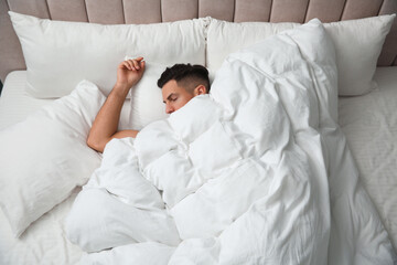 Handsome man sleeping under soft blanket in bed at home, above view