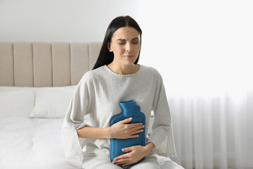 Woman using hot water bottle to relieve abdominal pain on bed at home