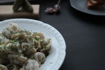 Folk traditional cuisine dishes dumplings sprinkled with fennel greens served with garlic bread in a white festive plate on a black dark background with a place for the text of the copyspace