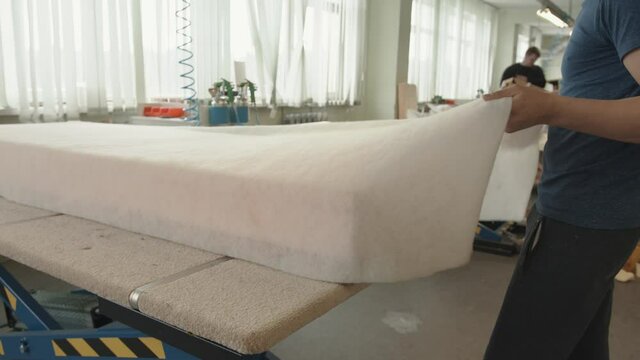 Professional worker in a repair and upholstery workshop does a new seat for a sofa from a large piece of foam rubber