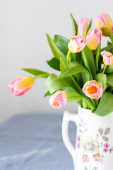 Beautiful spring bouquet of pink tulips in a jug on the table, flowers in a home interior
