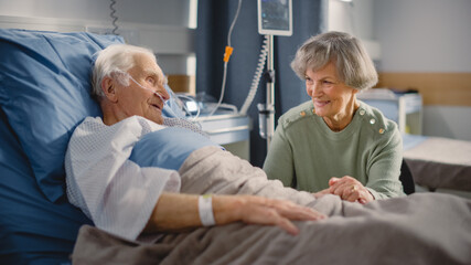 Hospital Ward: Elderly Man Resting in Bed, His Caring Beautiful Wife Supports Him Sitting Beside,...
