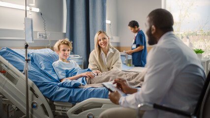 Hospital Ward: Handsome Young Boy Resting in Bed with Caring Mother Visits to Support Him, Friendly Doctor Talks, Gives Advice, Explains Test Results. Happy Smiling Patient Recovering after Sickness