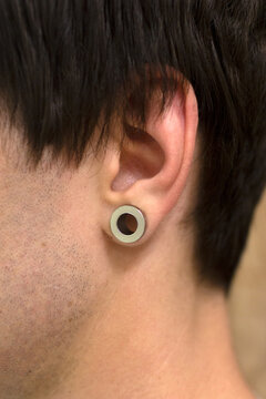 Tunnels in the ears. Male ear with a ring. Close-up. Silver color.