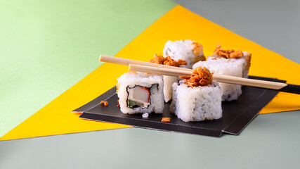 Set of sushi and rolls in black try with chopsticks on green  yellow background. Modern Japanese...