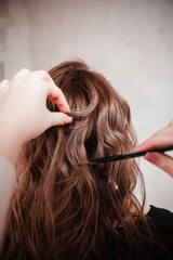 Naklejka premium the hairdresser makes the girl styling with an iron and a comb