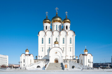 Fototapeta na wymiar Trinity christian orthodox cathedral in Magadan, Russia, white church with golden domes on sunny winter day with clear blue sky