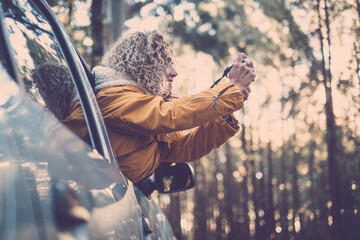 adventure vacation, holidays, travel, road trip and people concept - happy smiling young adult woman or young woman outside the car window taking picture to the forest woods nature
