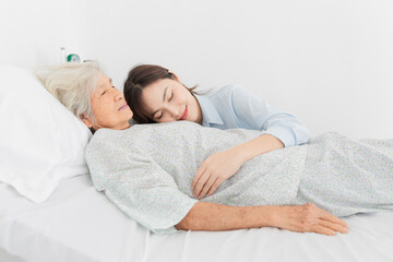 old asian patient rest on bed and young female rest face on her body, she sick and admit in hospital, they holding hand together and feeling happy, elderly healthcare