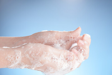 Fototapeta premium Woman hands in soapsuds, on blue background close-up.