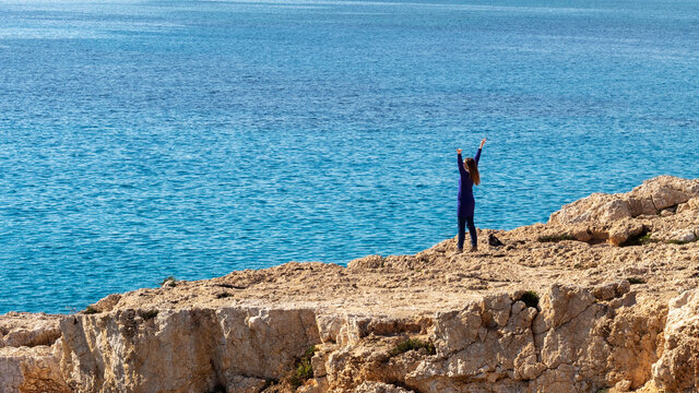 Happy woman enjoying freedom on the rocky shore on blue sea background.