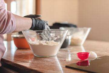 Una mujer que lleva guantes amasando la masa en un recipiente de cristal en la encimera de la cocina de su casa. Concepto de cocina casera. Hacer pizza y pan en casa.