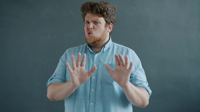 Portrait of emotional guy looking at camera with disgust and showing no gesture standing on gray background. Reactions and emotions concept.