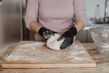 Una mujer amasando una masa de pizza sobre una tabla de madera mientras usa guantes de goma negros. Concepto de hacer pan en casa.