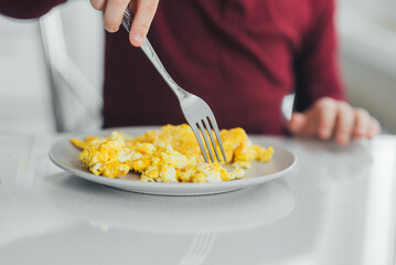 A child in the afternoon on a white light kitchen in a burgundy sweater eats an omelet