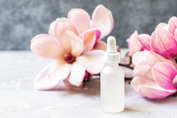 Serum with floral magnolia extracts for skincare. Nature cosmetics in glass bottle with a pipette and with flowers on grey background. Organic Spa Cosmetic With floral Ingredients. 