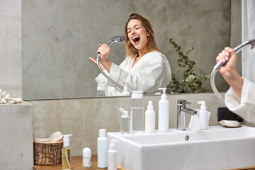 happy woman singing in bathtub using shower head having fun alone, after shower