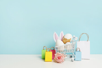 Easter eggs colorful in the shopping cart with bags on bright blue background. Festive concept.Copy space for Text.