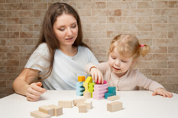 Obraz na płótnie Canvas Cute little girl and young mother woman playing with building blocks wooden toys on the table