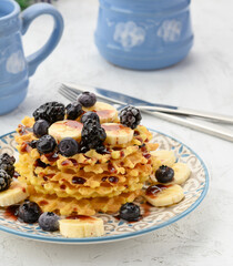stack of baked Belgian waffles on a round plate with berries on a white table, delicious breakfast