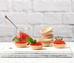 red caviar in a glass jar and round tartlets on a white table
