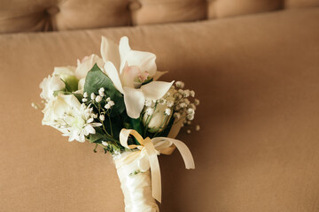Bridal wedding bouquet lying on modern brown sofa at home photo session studio. Stunning green white flowers roses wildflowers. Engagement between two lovoer people. Image with copy space.