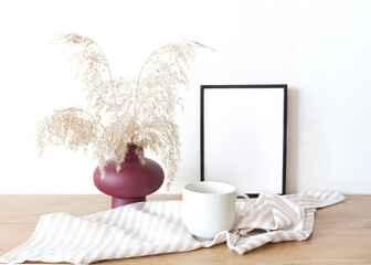Portrait empty wooden frame mockup with modern ceramic vase, dry grass and cup of coffee . Scandinavian interior, home design.
