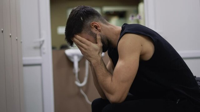 Portrait of exhausted or sad man sitting in gym locker room