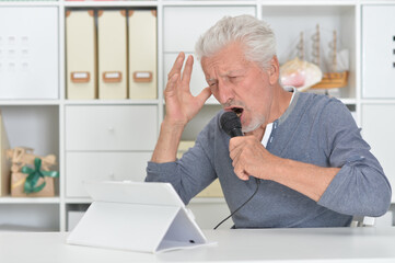 Emotional senior man singing karaoke with tablet at home