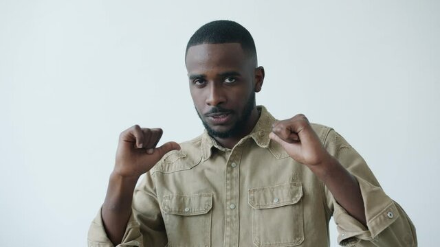 Slow motion of Afro-American guy pointing at himself with thumbs-up gesture and winking looking at camera on white background. People and lifestyle concept.