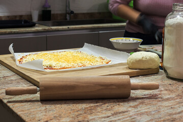 Encimera de cocina con una pizza casera sobre una tabla de madera junto a un rodillo y un gran tarro lleno de harina