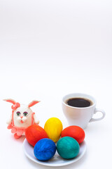 Fototapeta premium Hand-painted Easter eggs, a mug of coffee or hot chocolate and a homemade plasticine Easter bunny on a white