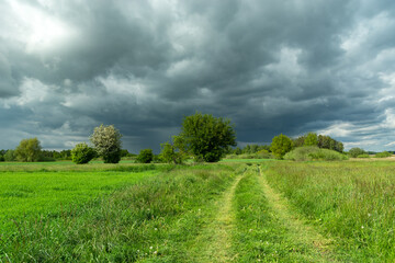 The road through a green meadow and dark rainy clouds