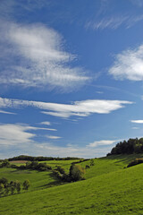 Obraz premium Ueber sanften Wiesenhuegeln ist ein freundlicher Schoenwetter-Hi
