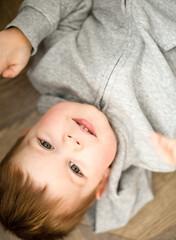 portrait of a nice little boy lying upside down on the wooden floor grey and brown colors 