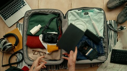 Man with paper notebook that says Adventure Time packs suitcase for international abroad travel. Neatly organized personal belongings. Top view social media concept. Personal items in bag