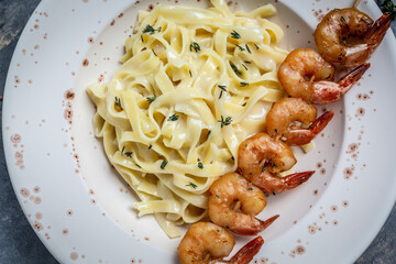 Close up Seafood tagliatelle pasta with grilled shrimps, bechamel sauce and thyme, fettuccine pasta. Italian food. Healthy diet seafood concept. Top view