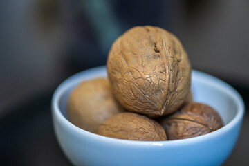 Heap, pile of whole walnuts in a round-shaped brown shell lie in a small white platter on black table on a dark blue green blurred bokeh background