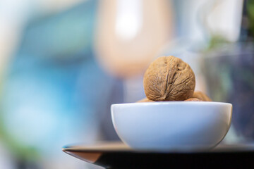 Heap of whole walnuts in a round-shaped brown shell lie in a small white platter on black plate on a blue green blurred bokeh background. Place for text