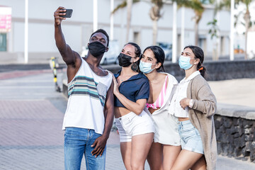 Company of diverse friends in masks taking selfie on street