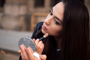 young woman touching up her makeup in the street