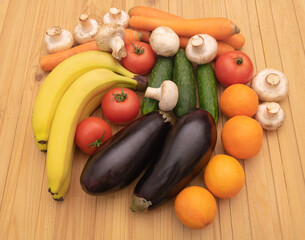 A mix of beneficial fruits and vegetables on wooden background - Bananas oranges eggplants tomatoes cucumbers carrots and mushrooms