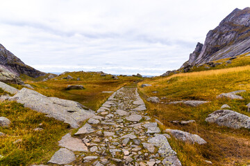 Stone slab hiking trail leads through rocky and rugged mountain landscape near the famous tourist hotspot Bunes Beach - Cloudy Autumn landscape on Bunes Beach Trail Head, Lofoten Islands, Norway