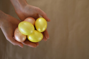 The girl holds in her hands Easter chicken eggs of yellow and pink color against the background of craft paper with a place for text. Selectiv focus