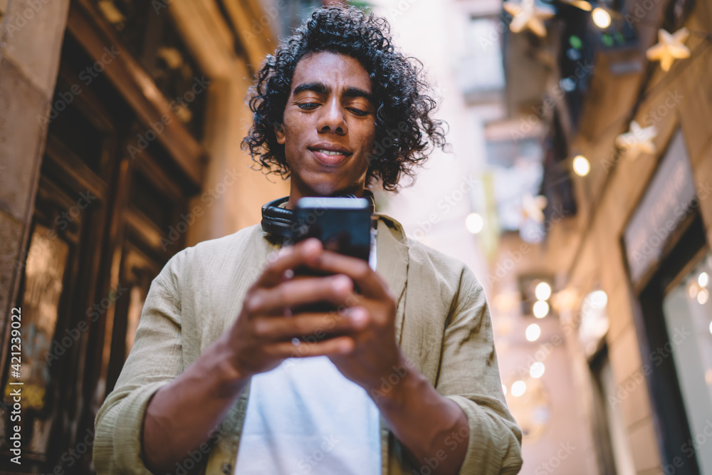 Poster handsome young male with curly hair using mobile phone for sending messages and text email, hispanic