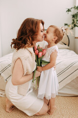 Portrait of a pretty beautiful gentle cute tender red-haired mother and daughter together sniffing a spring bouquet of flowers tulips presented for the holidays Mother's Day and March 8